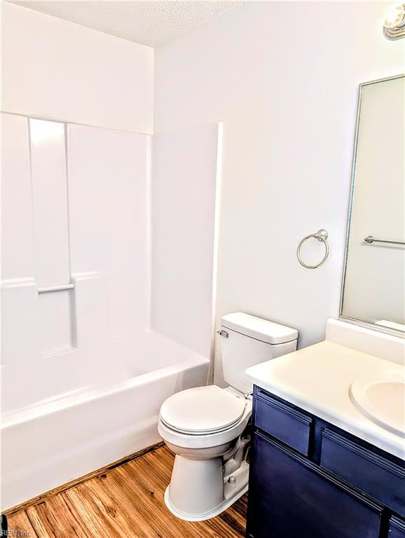 full bathroom with hardwood / wood-style floors, vanity, shower / washtub combination, toilet, and a textured ceiling