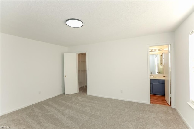 unfurnished bedroom featuring ensuite bath, a walk in closet, a closet, and light colored carpet