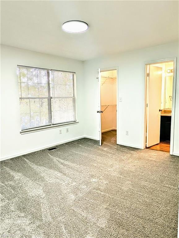 unfurnished bedroom featuring carpet flooring, ensuite bathroom, a spacious closet, and a closet