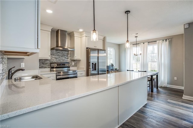 kitchen with light stone counters, pendant lighting, stainless steel appliances, and wall chimney range hood