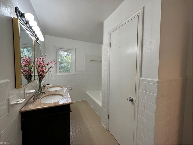 full bath with double vanity, tile walls, a sink, and a wainscoted wall
