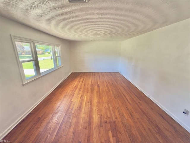 spare room with baseboards and wood finished floors