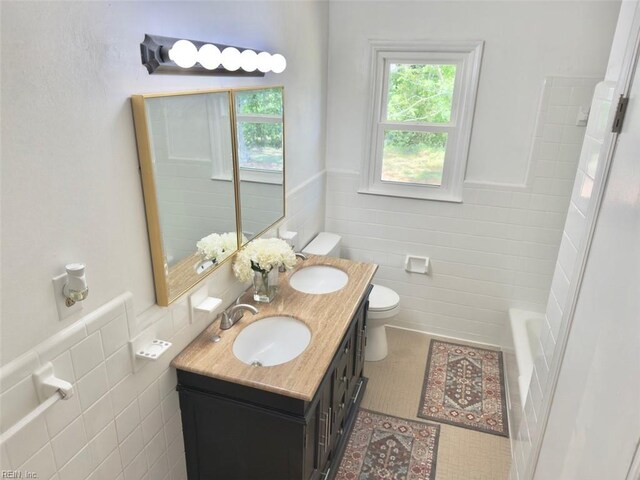 bathroom featuring a sink, a wainscoted wall, toilet, and tile walls