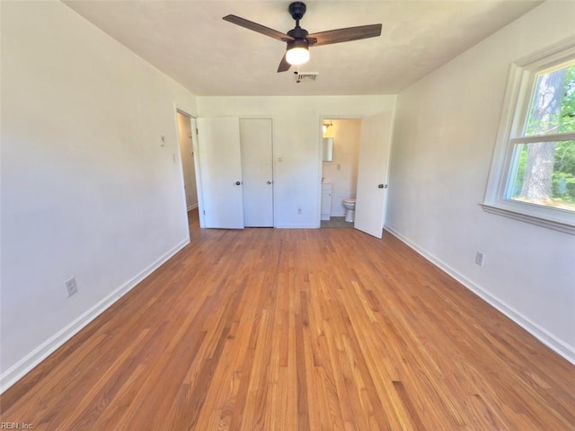 unfurnished bedroom with visible vents, connected bathroom, baseboards, and wood finished floors