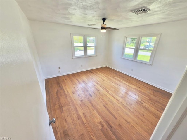empty room with a ceiling fan, baseboards, visible vents, and wood finished floors
