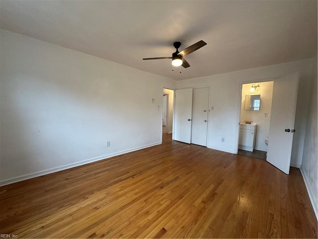 unfurnished bedroom featuring baseboards, a ceiling fan, ensuite bathroom, and wood finished floors