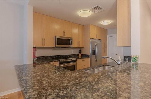 kitchen with kitchen peninsula, appliances with stainless steel finishes, light brown cabinetry, and dark stone countertops