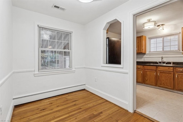 unfurnished dining area with sink, a baseboard radiator, and light hardwood / wood-style flooring