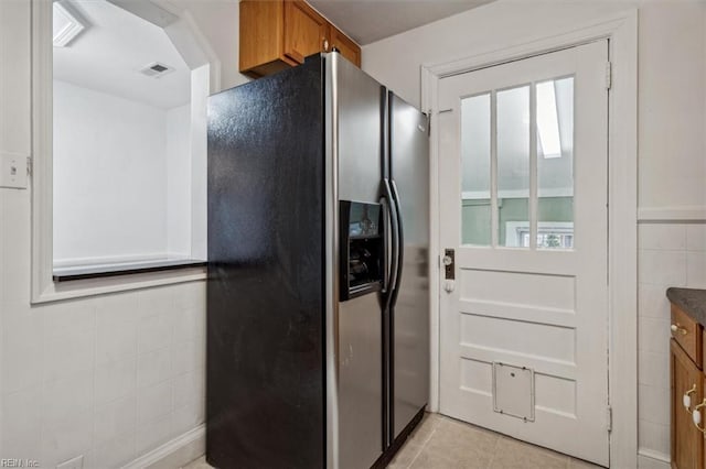 kitchen with stainless steel refrigerator with ice dispenser, light tile patterned floors, and tile walls