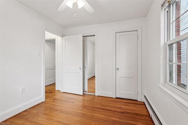 unfurnished bedroom with ceiling fan, light hardwood / wood-style floors, baseboard heating, and multiple closets