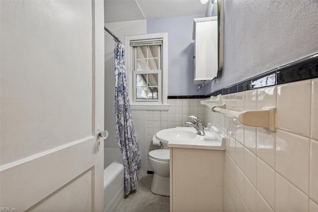 full bathroom with shower / bathtub combination with curtain, tile patterned flooring, toilet, vanity, and tile walls