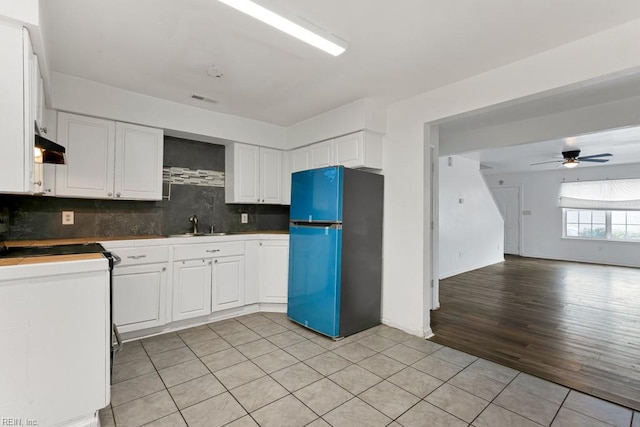 kitchen with white cabinetry, black fridge, ceiling fan, and light hardwood / wood-style floors