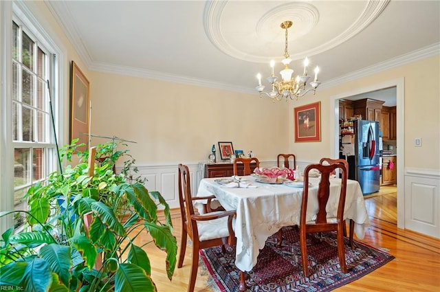 dining area with light hardwood / wood-style floors, a wealth of natural light, ornamental molding, and a notable chandelier