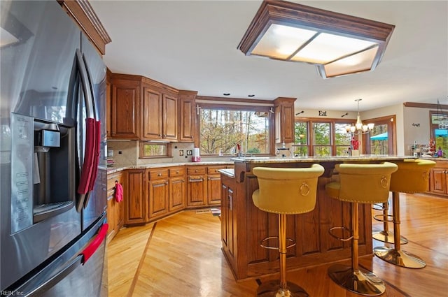 kitchen with stainless steel fridge with ice dispenser, a notable chandelier, decorative light fixtures, a breakfast bar, and a kitchen island