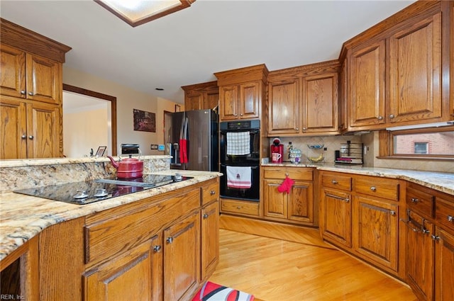 kitchen with light stone countertops, decorative backsplash, light wood-type flooring, and black appliances