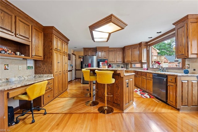 kitchen featuring a center island, black dishwasher, light stone counters, a kitchen bar, and light wood-type flooring