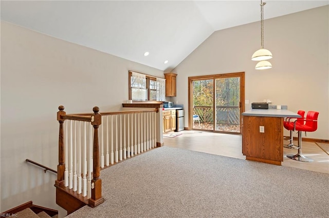 interior space featuring light carpet, a kitchen breakfast bar, decorative light fixtures, and lofted ceiling