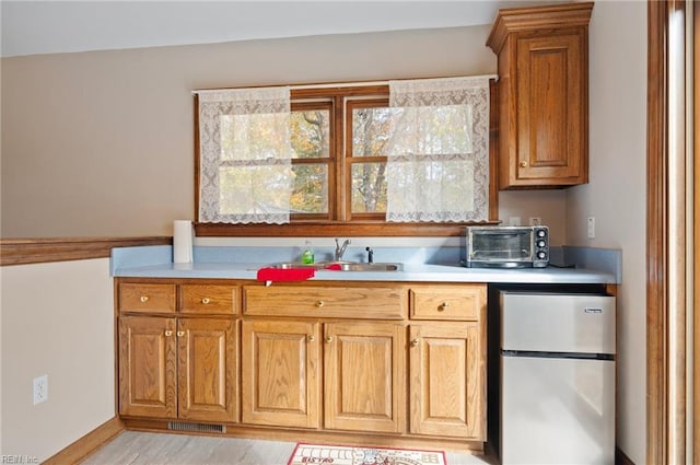 kitchen featuring stainless steel refrigerator, sink, and light hardwood / wood-style floors