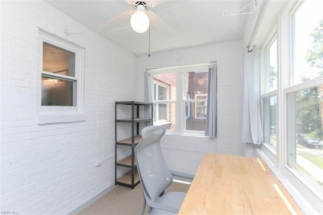 home office with a wealth of natural light, ceiling fan, and brick wall