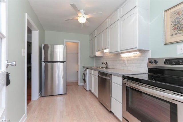 kitchen with appliances with stainless steel finishes, light wood-type flooring, backsplash, white cabinets, and washer / dryer