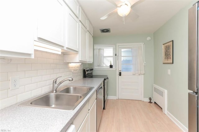 kitchen with white cabinets, sink, light wood-type flooring, tasteful backsplash, and radiator heating unit