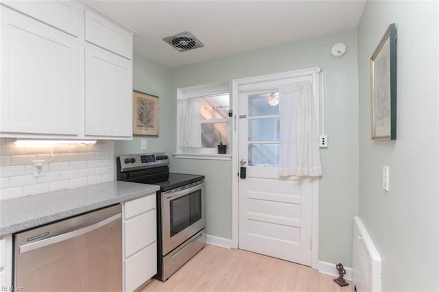 kitchen with white cabinets, light stone countertops, appliances with stainless steel finishes, tasteful backsplash, and light hardwood / wood-style floors