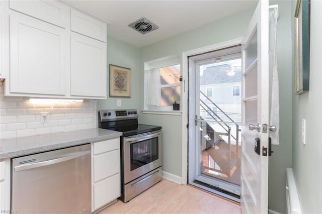 kitchen with light stone countertops, light wood-type flooring, appliances with stainless steel finishes, tasteful backsplash, and white cabinetry