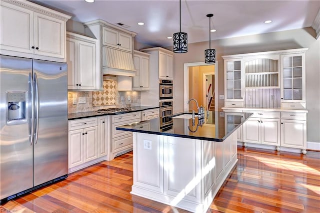 kitchen featuring sink, stainless steel appliances, light hardwood / wood-style flooring, decorative light fixtures, and a center island with sink