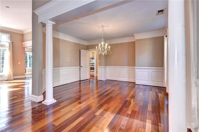 unfurnished dining area with decorative columns, crown molding, hardwood / wood-style floors, and an inviting chandelier