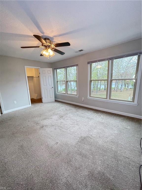 unfurnished bedroom with ceiling fan, a spacious closet, a textured ceiling, carpet floors, and a closet