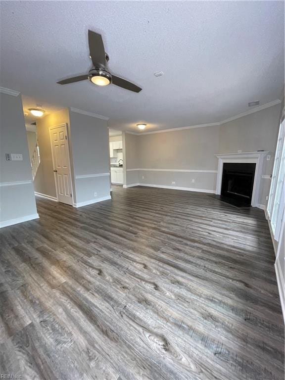 unfurnished living room with ceiling fan, dark hardwood / wood-style flooring, ornamental molding, and a textured ceiling