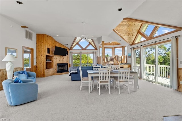 carpeted dining area featuring wood walls, plenty of natural light, ceiling fan, and a fireplace