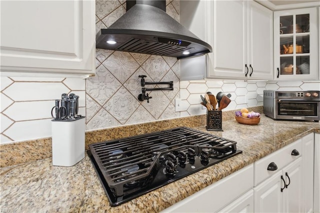 kitchen featuring wall chimney exhaust hood, black gas stovetop, white cabinetry, and backsplash