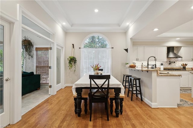 dining area featuring a tray ceiling, sink, light hardwood / wood-style flooring, and ornamental molding