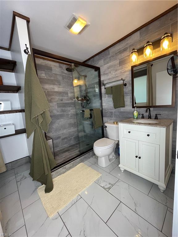 bathroom with vanity, a shower with door, toilet, and tile walls