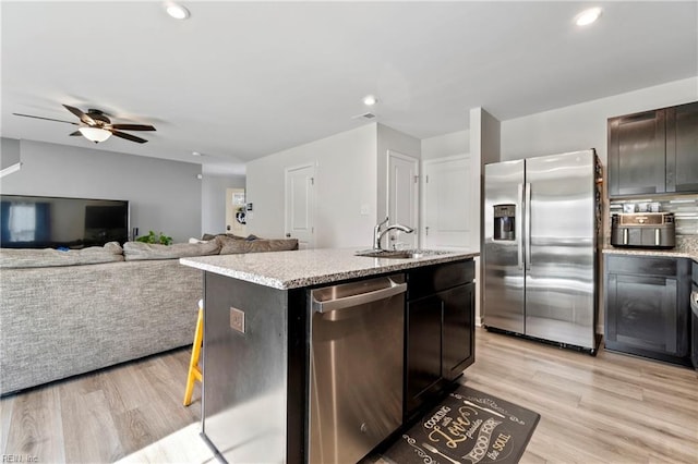 kitchen with ceiling fan, an island with sink, stainless steel appliances, and light hardwood / wood-style floors