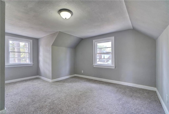 bonus room with vaulted ceiling, plenty of natural light, carpet floors, and a textured ceiling