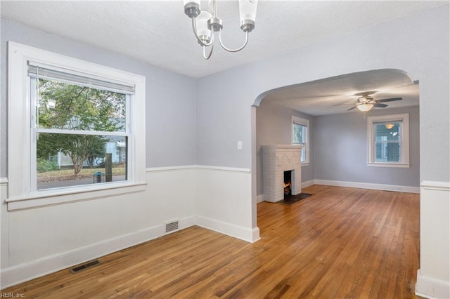 unfurnished living room featuring a textured ceiling, a fireplace, wood-type flooring, and ceiling fan with notable chandelier