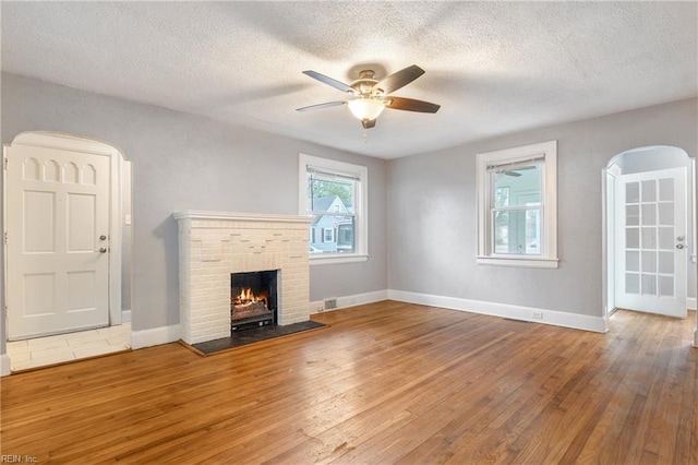 unfurnished living room featuring ceiling fan, a fireplace, wood-type flooring, and a textured ceiling