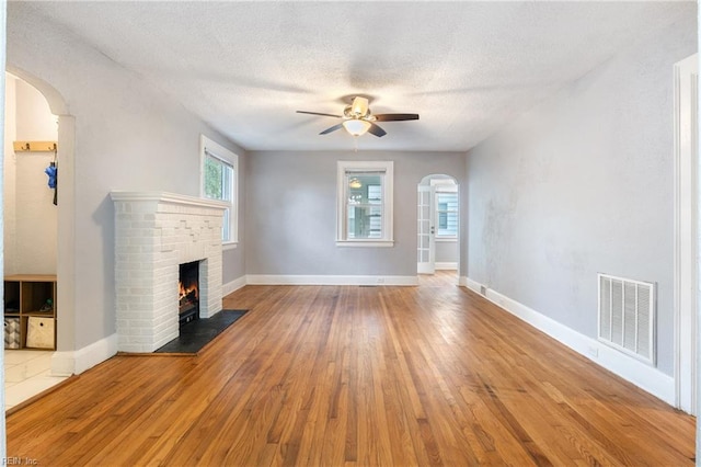 unfurnished living room with ceiling fan, wood-type flooring, a textured ceiling, and a brick fireplace