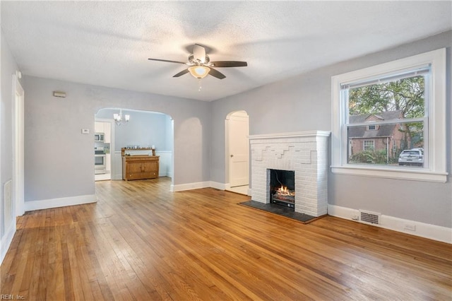 unfurnished living room featuring hardwood / wood-style floors, ceiling fan, a textured ceiling, and a brick fireplace