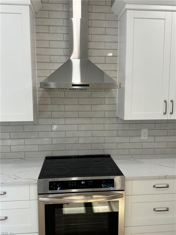 kitchen featuring white cabinetry, light stone countertops, wall chimney range hood, and stainless steel stove