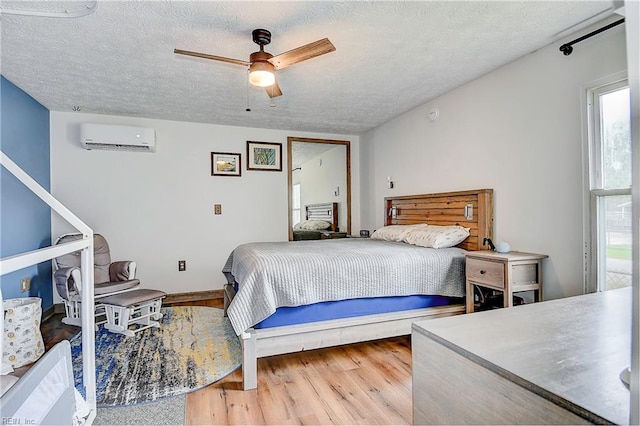 bedroom with hardwood / wood-style flooring, ceiling fan, an AC wall unit, and a textured ceiling