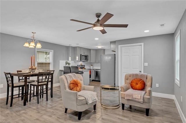 living room featuring ceiling fan with notable chandelier and light hardwood / wood-style flooring