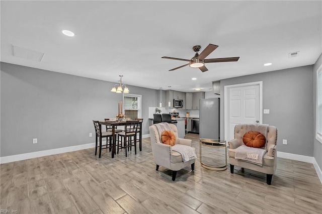 living room with ceiling fan with notable chandelier and light hardwood / wood-style floors