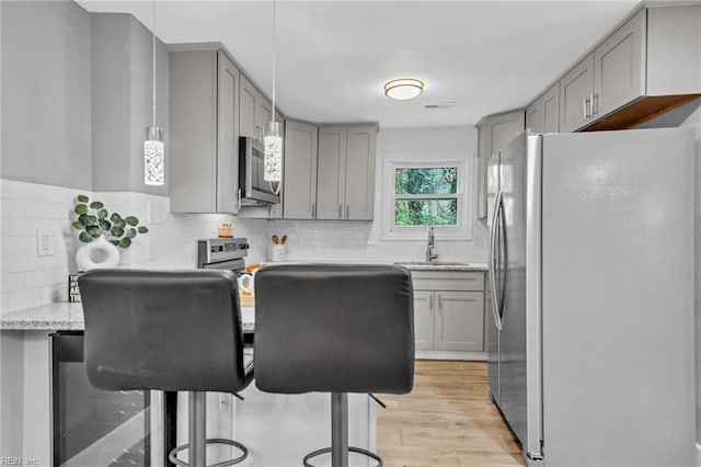 kitchen featuring a kitchen breakfast bar, sink, gray cabinets, light hardwood / wood-style floors, and stainless steel appliances