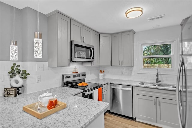 kitchen with light stone countertops, sink, hanging light fixtures, light hardwood / wood-style flooring, and appliances with stainless steel finishes