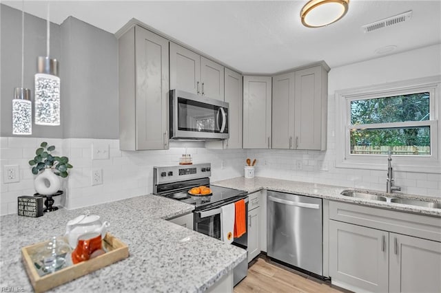 kitchen with backsplash, sink, light wood-type flooring, light stone countertops, and appliances with stainless steel finishes