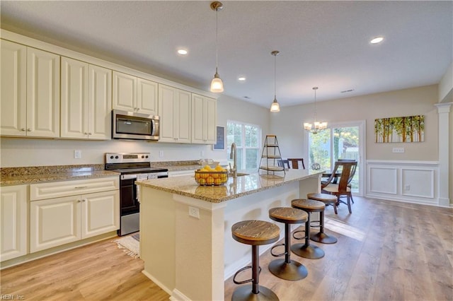 kitchen featuring a breakfast bar, a kitchen island with sink, appliances with stainless steel finishes, decorative light fixtures, and light stone counters