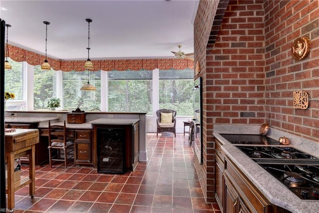 kitchen featuring light stone counters, brick wall, pendant lighting, black gas cooktop, and wine cooler